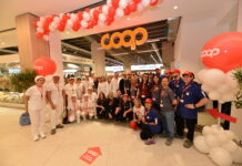 Group of COOP staff and volunteers posing for a photo at a store opening, under red-and-white balloons and a bright COOP sign.