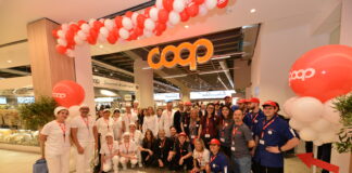Group of COOP staff and volunteers posing for a photo at a store opening, under red-and-white balloons and a bright COOP sign.