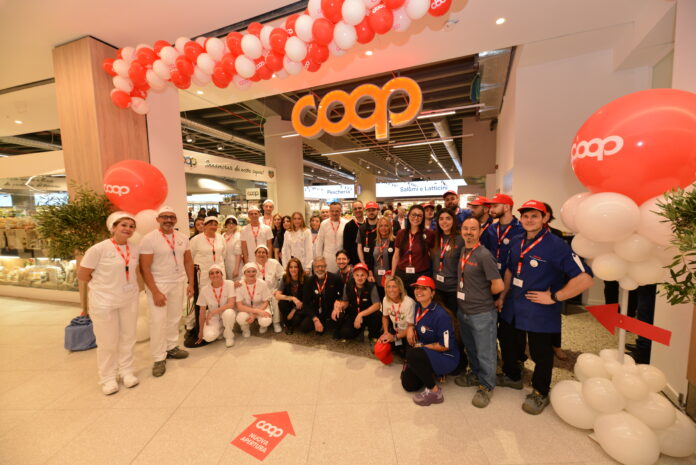 Group of COOP staff and volunteers posing for a photo at a store opening, under red-and-white balloons and a bright COOP sign.