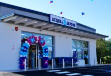 Acqua & Sapone raggiunge quota 886 punti vendita con tre nuove aperture Exterior of an Acqua & Sapone store with a colorful balloon arch at the entrance and shopping carts outside, bright blue sky overhead.