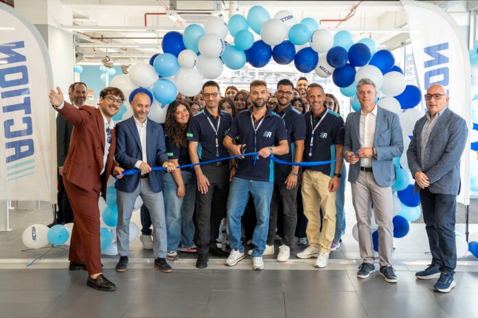 Group of employees at a ribbon-cutting ceremony with blue and white balloons in a bright showroom.