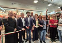 Group of people at a ribbon-cutting ceremony indoors, holding a green-white-red ribbon together.