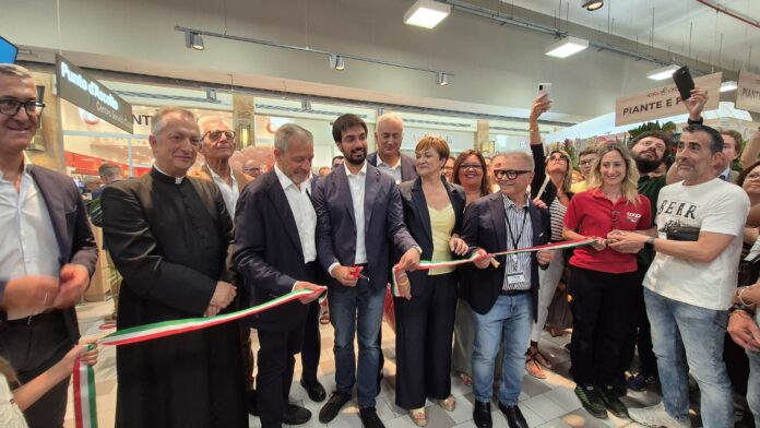 Group of people at a ribbon-cutting ceremony indoors, holding a green-white-red ribbon together.