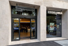 Esselunga supermarket entrance with glass doors and a 'Supermarket' sign above on a beige stone facade.