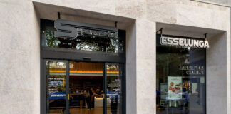 Esselunga supermarket entrance with glass doors and a 'Supermarket' sign above on a beige stone facade.