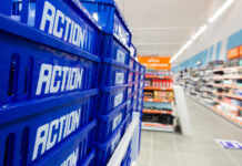 Stack of blue plastic crates labeled 'ACTION' in a store aisle foregrounding the scene's depth and shelves in the background.