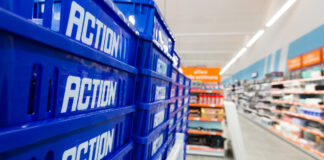 Stack of blue plastic crates labeled 'ACTION' in a store aisle foregrounding the scene's depth and shelves in the background.