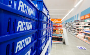 Stack of blue plastic crates labeled 'ACTION' in a store aisle foregrounding the scene's depth and shelves in the background.