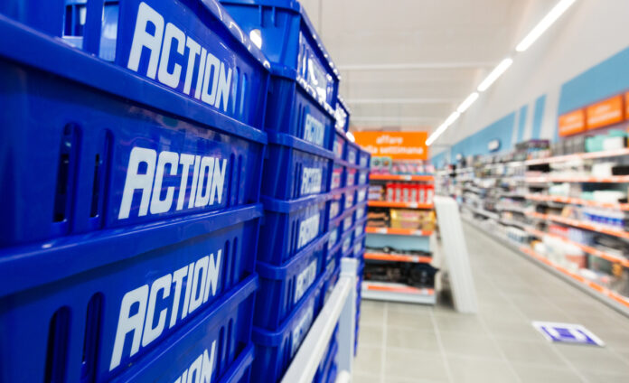 Stack of blue plastic crates labeled 'ACTION' in a store aisle foregrounding the scene's depth and shelves in the background.