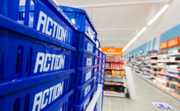 Action rafforza la rete in Emilia-Romagna con il quarto store nel Bolognese Blue plastic crates labeled 'ACTION' stacked along a supermarket aisle wall.