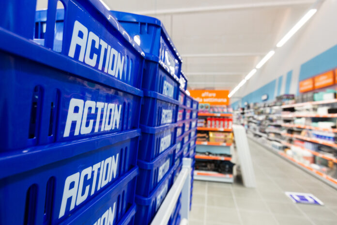 Blue plastic crates labeled 'ACTION' stacked along a supermarket aisle wall.