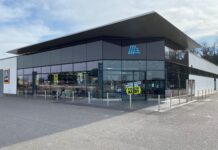 Modern ALDI supermarket exterior with glass storefront and blue logo on a cloudy day.