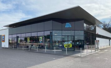 Il discount evolve, ALDI sceglie di restare discount Modern ALDI supermarket exterior with glass storefront and blue logo on a cloudy day.