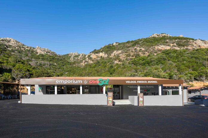 Front of a small storefront with a sign reading 'emporium' against a hillside and clear blue sky.