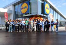 Lidl consolida la presenza in provincia di Napoli con un nuovo store Group of people at a Lidl store during a ribbon-cutting ceremony with blue ribbon and yellow-red balloons outside the entrance.