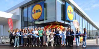 Group of people at a Lidl store during a ribbon-cutting ceremony with blue ribbon and yellow-red balloons outside the entrance.