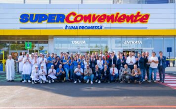 Group of supermarket staff posing in front of a SuperConveniente store entrance.