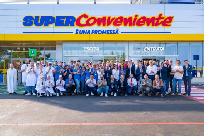 Group of supermarket staff posing in front of a SuperConveniente store entrance.