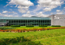 Modern glass-front corporate building with a landscaped lawn and flower beds in front, and a large 'Superstore' sign on the right.