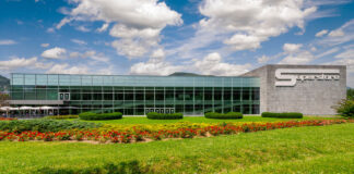 Modern glass-front corporate building with a landscaped lawn and flower beds in front, and a large 'Superstore' sign on the right.