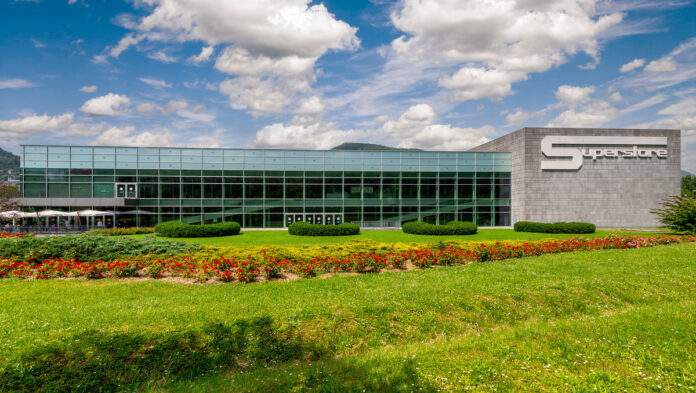 Modern glass-front corporate building with a landscaped lawn and flower beds in front, and a large 'Superstore' sign on the right.