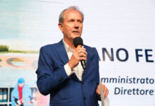 Conad Centro Nord chiude il 2025 a 2,19 miliardi e vara un piano da 382 milioni Man in a blue suit speaks into a handheld microphone on stage, background shows text and graphics behind him.