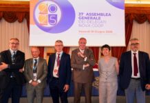 Six professionals in suits posing on a stage in front of a banner at a formal conference.