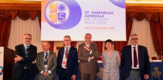 Six professionals in suits posing on a stage in front of a banner at a formal conference.