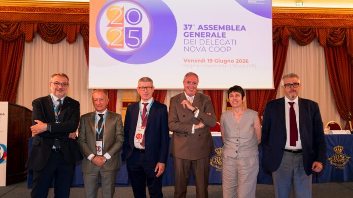 Six professionals in suits posing on a stage in front of a banner at a formal conference.