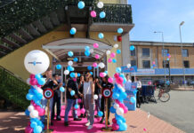Group of people at a ribbon-cutting ceremony under blue, pink, and white balloons on a pink carpet outside a building.