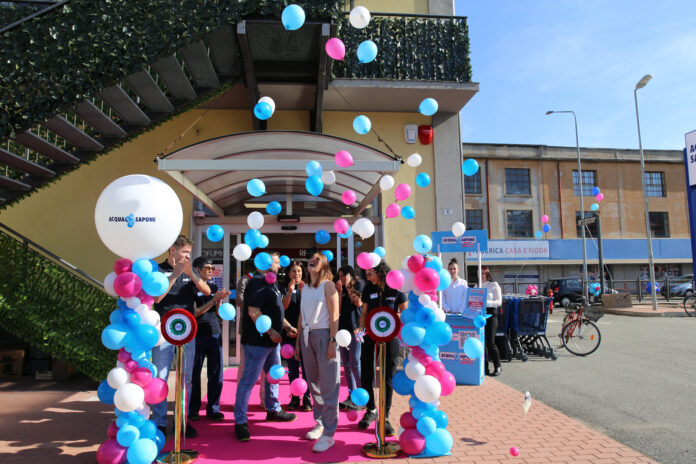 Group of people at a ribbon-cutting ceremony under blue, pink, and white balloons on a pink carpet outside a building.
