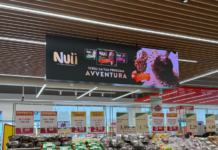 Produce aisle in a supermarket showing kiwis, kiwifruit, avocados and pineapples with a Nuii ice cream ad banner overhead.