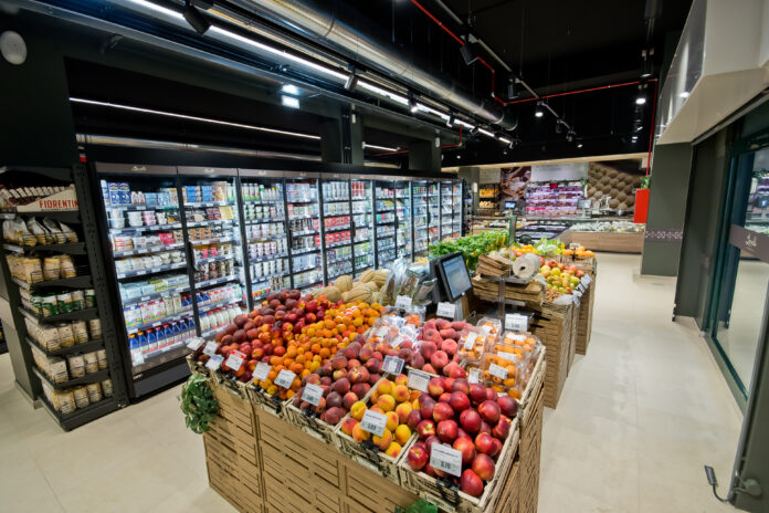 Nuovo punto vendita Borello_Venaria Reale 02 Fresh fruit display in wooden crates at a modern supermarket, with glass-door refrigerated sections behind it.