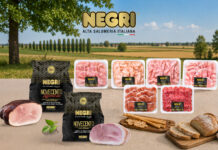 Assorted NEGRI Italian deli meats in plastic trays and black packaging on a wooden table, countryside backdrop with green fields and blue sky.
