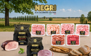 Negri Salumi punta sulla filiera italiana per valorizzare il mercato Assorted NEGRI Italian deli meats in plastic trays and black packaging on a wooden table, countryside backdrop with green fields and blue sky.