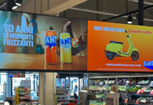 Store interior with a large double-panel advertisement: left shows Fanta cans, right shows a yellow scooter on an orange background.