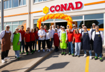 Conad Adriatico rafforza il presidio nel Barese con il restyling di Polignano Group photo of Conad staff and volunteers under an orange balloon arch at a store opening, wearing colorful aprons and uniforms.