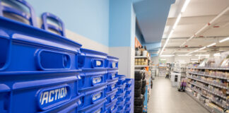 Blue stacked plastic bins labeled ACTION line the left foreground of a bright store aisle, with shelves of products visible on the right.
