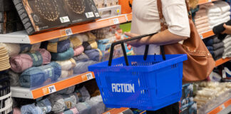 Action rafforza la presenza a Roma con il nuovo punto vendita Collatina Person with a brown bag pushing a blue shopping basket along a yarn aisle filled with colorful skeins and price tags on orange shelves in a store.