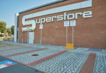 Exterior view of a brick building with a large white 'SUPERSTORE' sign on the wall, with handicap parking signs and bollards in the foreground.