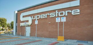 Exterior view of a brick building with a large white 'SUPERSTORE' sign on the wall, with handicap parking signs and bollards in the foreground.