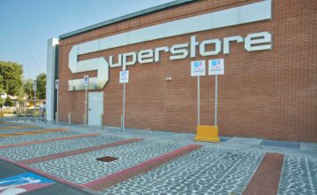 Esselunga trasforma lo storico supermercato di Massa in un superstore Exterior view of a brick building with a large white 'SUPERSTORE' sign on the wall, with handicap parking signs and bollards in the foreground.