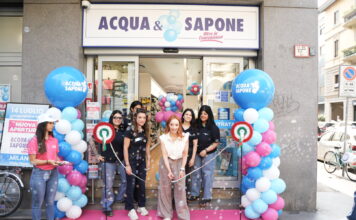 Ribbon-cutting ceremony outside Acqua & Sapone store with pink carpet and blue/pink balloons and staff members smiling.