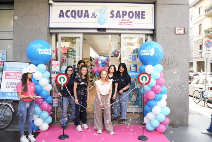 Ribbon-cutting ceremony outside Acqua & Sapone store with pink carpet and blue/pink balloons and staff members smiling.