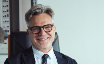 Dit, bilancio 2025 positivo: ricavi a 19,1 milioni e focus sulla marca privata Smiling mature man with gray hair and glasses, wearing a dark suit and tie in an office setting.