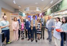 Benessity Conad debutta a Firenze con il primo punto vendita in Italia Group of professionals in business and casual attire cutting a ribbon in a store aisle during a grand opening ceremony.