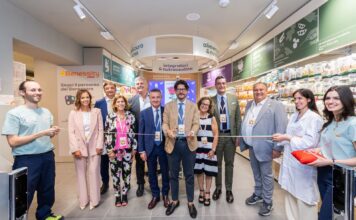 Group of professionals in business and casual attire cutting a ribbon in a store aisle during a grand opening ceremony.
