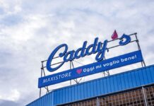 Store sign reading "Caddy's" with a blue banner below that says "MAXISTORE ? Oggi mi voglio bene!" against a cloudy sky.
