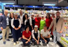 Group of supermarket staff posing in the dairy aisle with yogurt and cheese behind them.