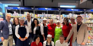 Conad City riapre a Castel di Lama con un punto vendita rinnovato Group of supermarket staff posing in the dairy aisle with yogurt and cheese behind them.
